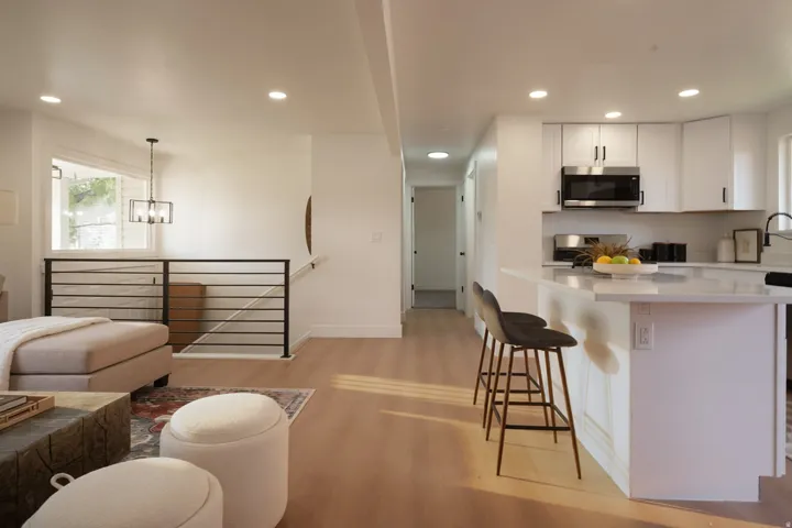 Recessed lighting, wood-finish flooring, white cabinetry with black hardware, stainless steel microwave, and a kitchen island with a light-colored countertop