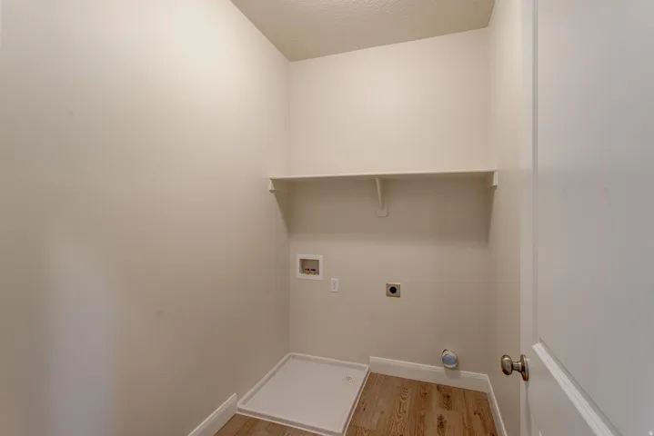 Laundry area with wood-finish flooring, a wall-mounted shelf, and neutral-toned walls