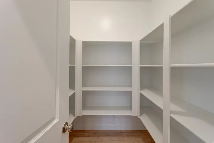 Walk-in pantry featuring extensive white shelving and wood-finish flooring