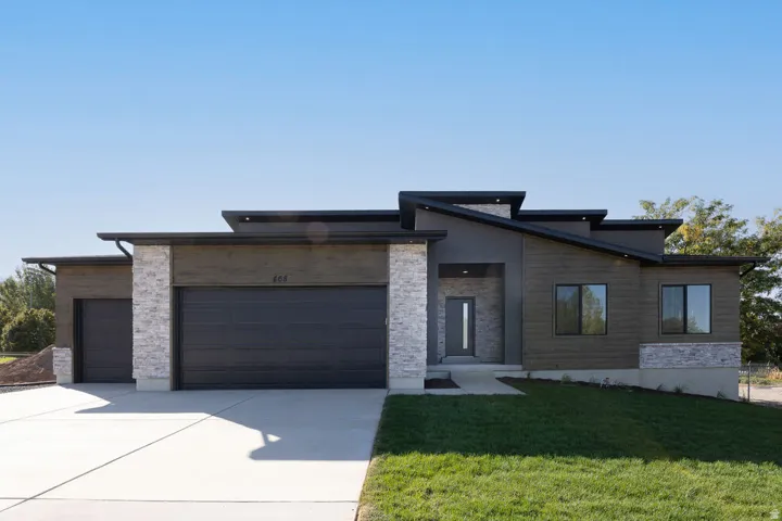 Modern architectural exterior featuring a multi-level roofline, stone veneer accents, wood-finish siding, and a prominent two-car garage