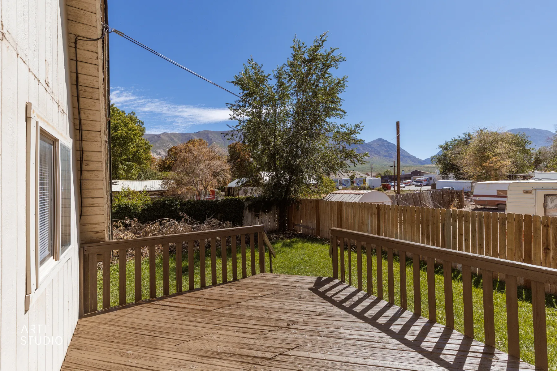 Expansive wooden deck with railing, leading to a grass yard with a wooden fence