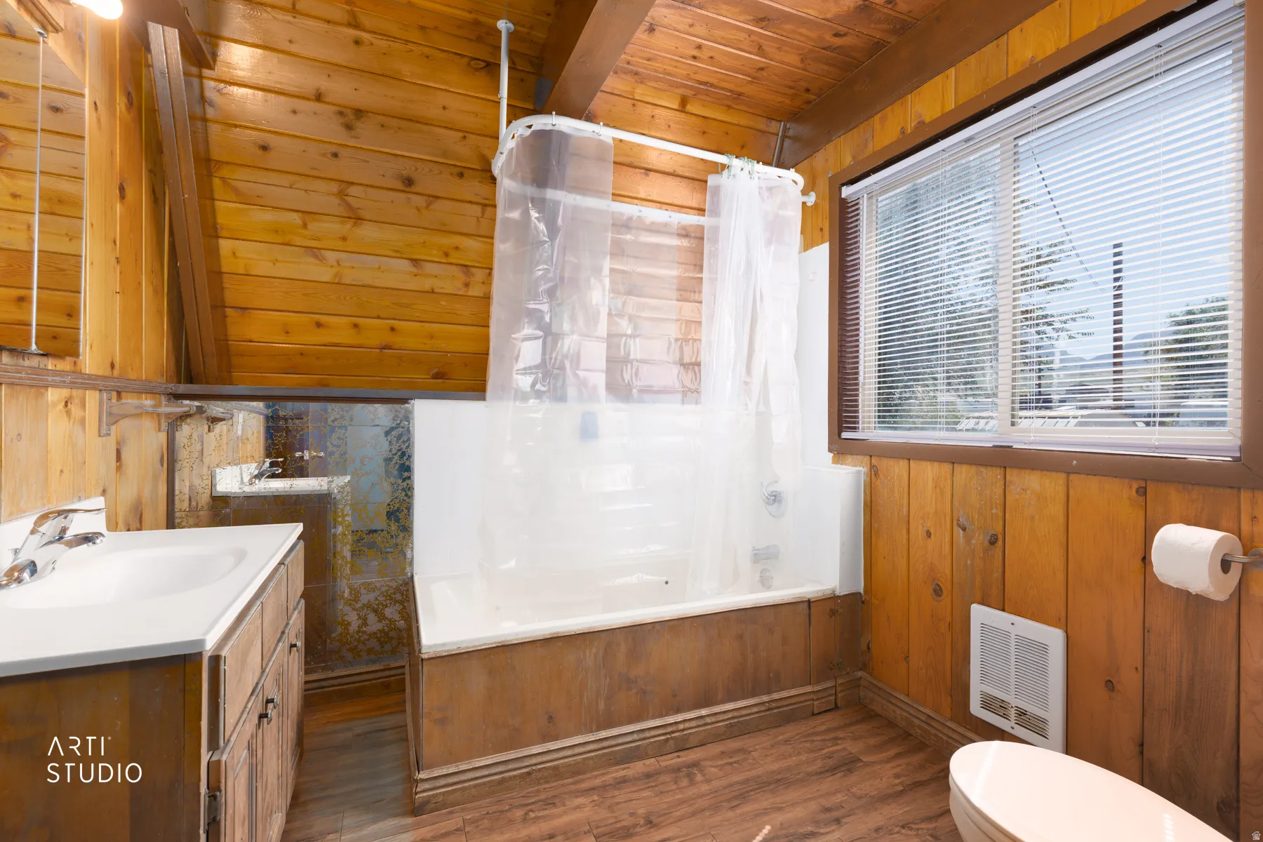 Vaulted wood-paneled ceiling, wood-finish flooring, wood vanity with integrated sink, built-in bathtub, and window with horizontal blinds