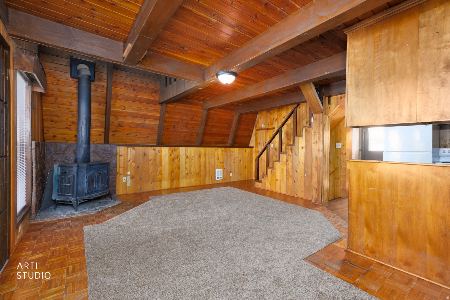 Wood-paneled room featuring a wood-burning stove with a stone surround, exposed wood beams, and a wood staircase