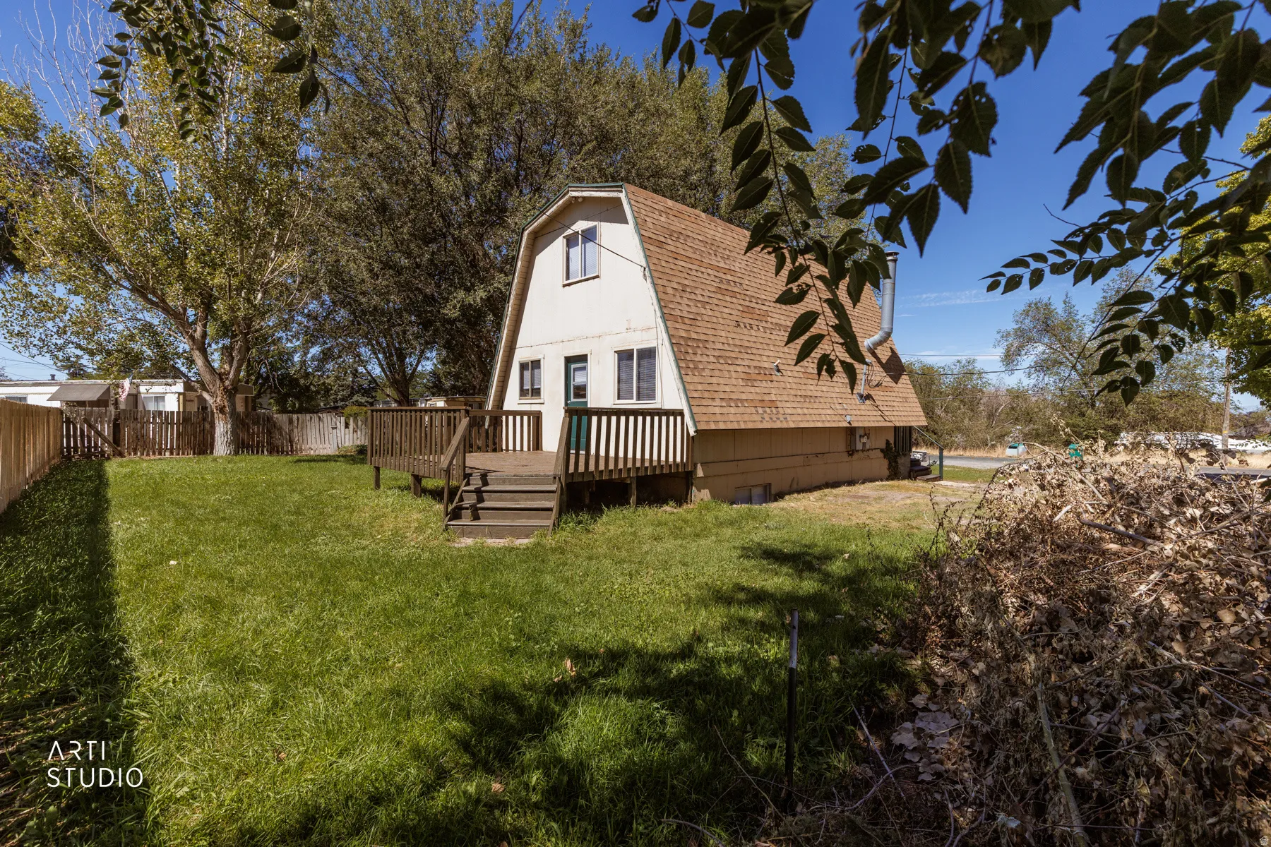 Gambrel-style residence featuring a wooden deck, sloped shingle roof, and a fenced backyard with a grass lawn