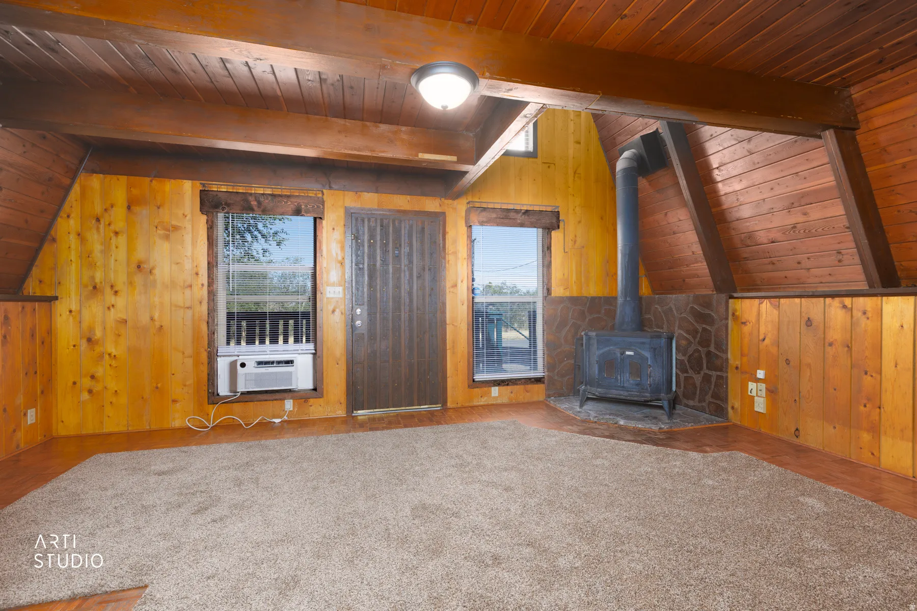 Vaulted wood-paneled ceilings, prominent wood beams, a wood-burning stove, stone hearth, and wood-paneled walls