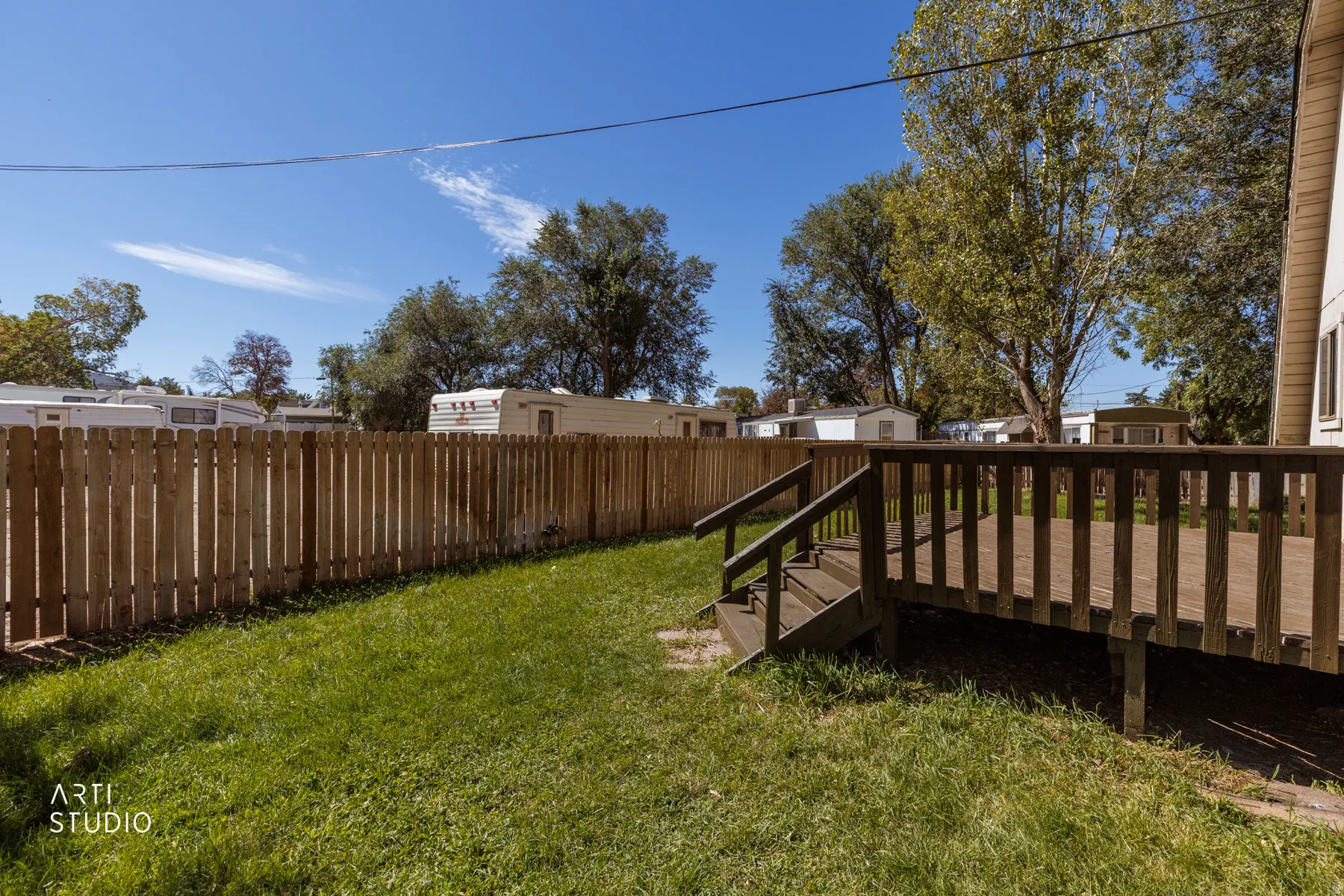 Expansive wood deck with railing and stairs, surrounded by a wood picket fence, and a grass lawn