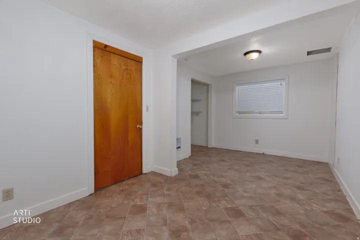 Warm wood door with a silver knob, neutral tiled flooring, white walls, and a window with horizontal blinds