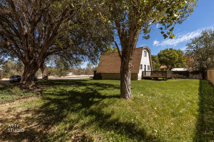 Expansive grassy yard with mature trees, a wood deck, a partial wood fence, and a dormer window on the property