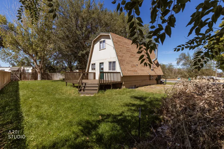 Gambrel-style residence featuring a wooden deck, sloped shingle roof, and a fenced backyard with a grass lawn