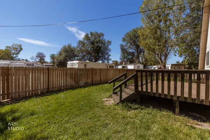 Expansive wood deck with railing and stairs, surrounded by a wood picket fence, and a grass lawn
