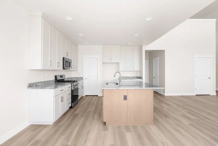 Kitchen featuring white cabinetry, stainless steel appliances, granite countertops, and an island with a stainless steel sink