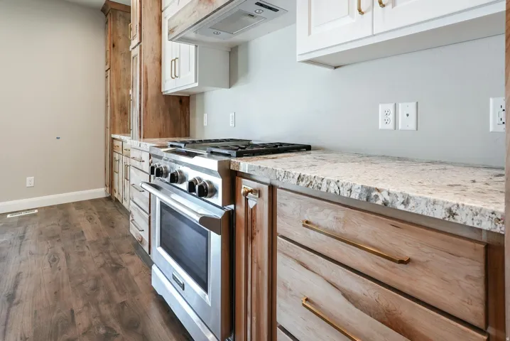 Stainless steel range with a built-in oven, light-toned countertops, wood-finish flooring, and cabinetry featuring both wood-tone and white finishes