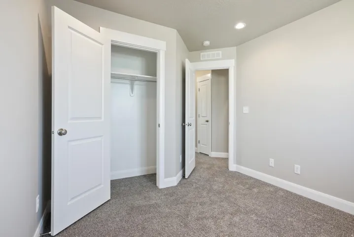 Recessed ceiling lighting, light gray wall paint, white trim, gray carpet flooring, and a closet with white bi-fold doors