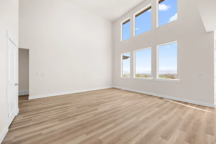 Vaulted ceiling with multiple large windows, light wood-finish flooring, and white wall finishes
