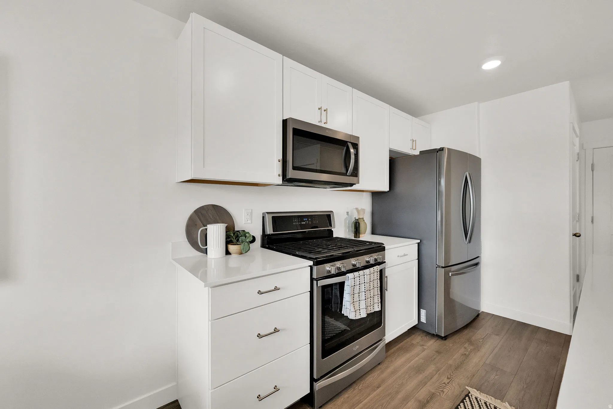 White cabinetry, stainless steel appliances, wood-finish flooring, recessed lighting, and white countertops