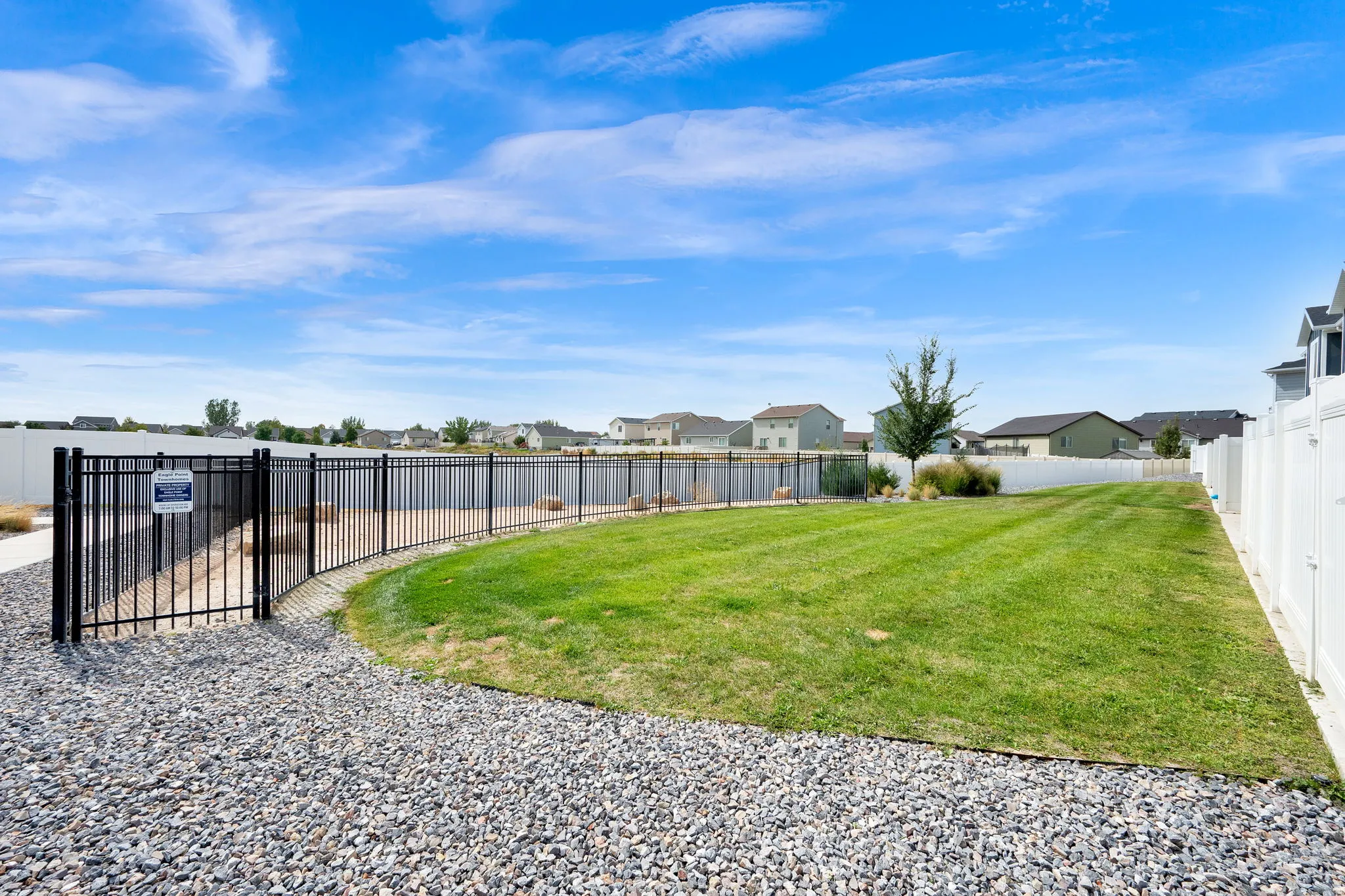 Expansive green space featuring a large lawn area, a black metal fence with a gate (Dog Walk), a white privacy fence, and a gravel ground cover