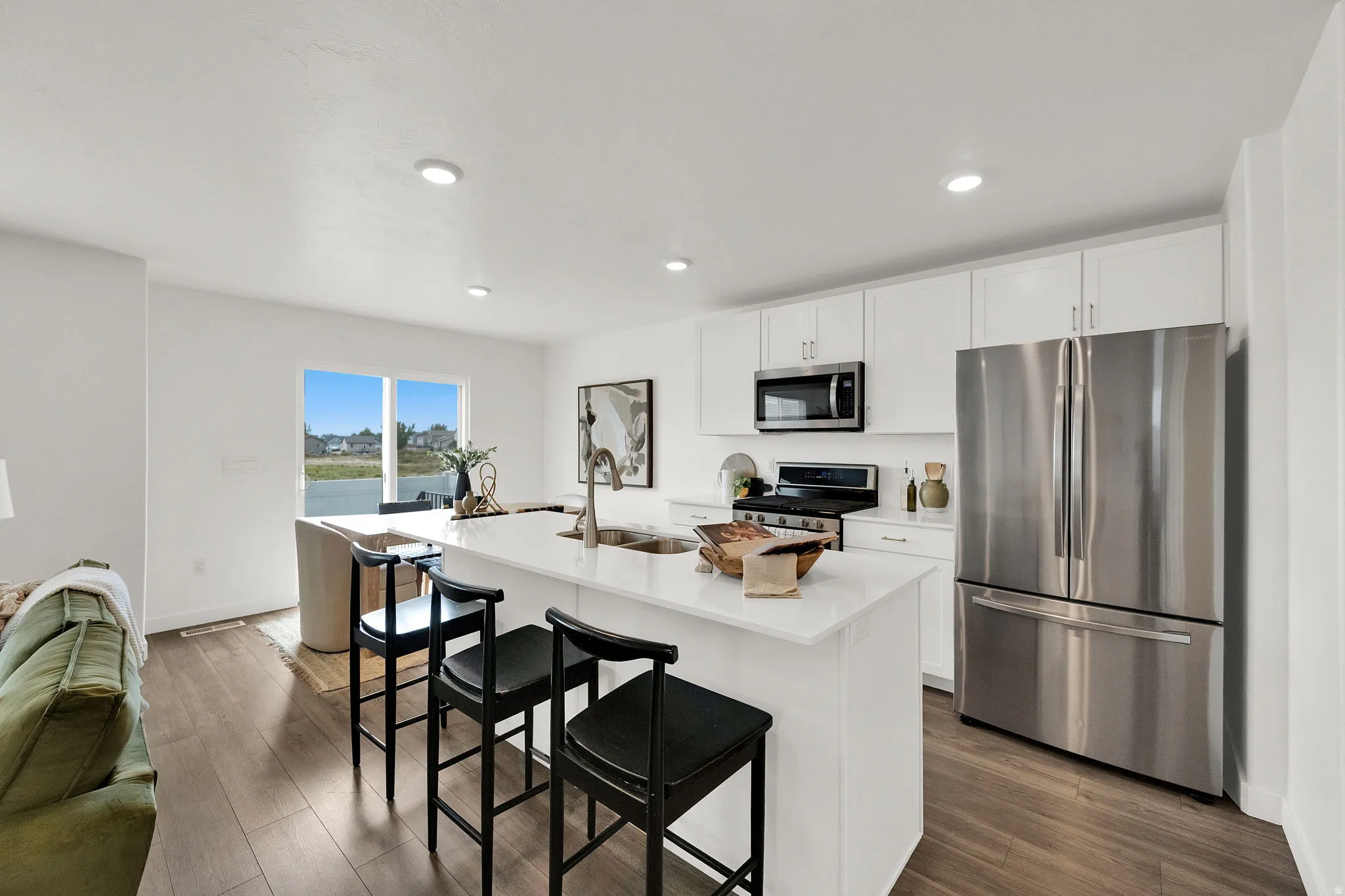 Open-concept kitchen with white cabinetry, stainless steel appliances, a center island with countertop seating, and wood-finish flooring