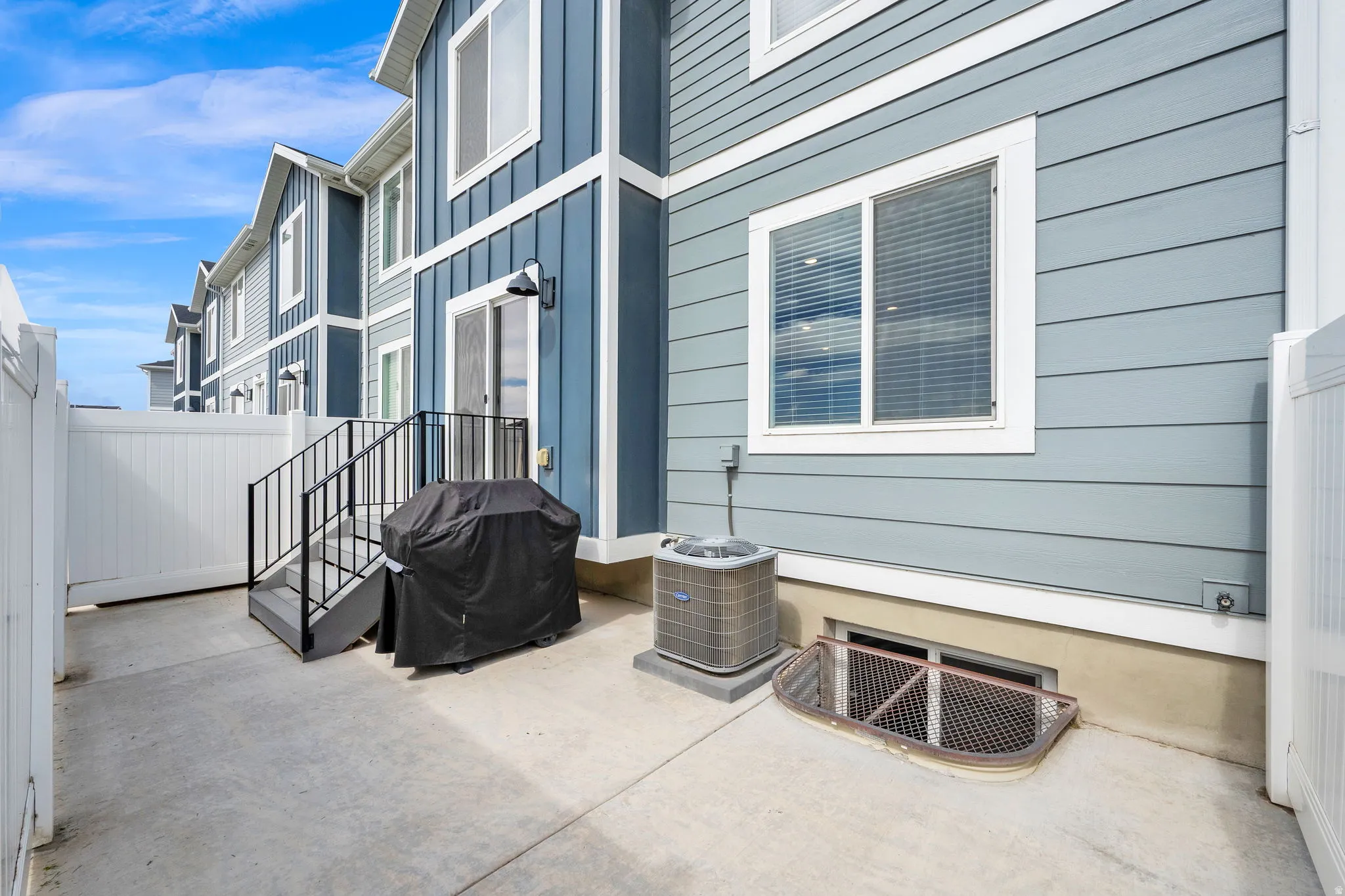 Concrete patio area with a white privacy fence, exterior siding, and a sliding glass door