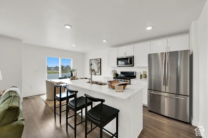 Open-concept kitchen with white cabinetry, stainless steel appliances, a center island with countertop seating, and wood-finish flooring