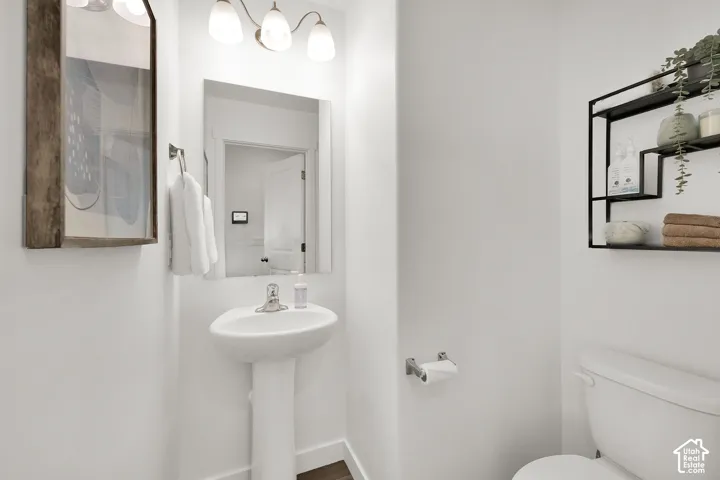 Pedestal sink, wall-mounted mirror, overhead vanity lighting, and a wall-mounted shelving unit