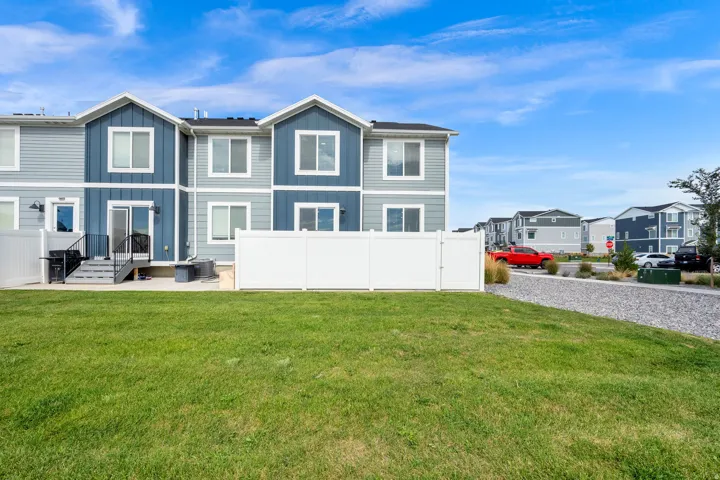 Rear exterior featuring a patio with steps, sliding glass door access, white privacy fencing, and an expansive grassy area