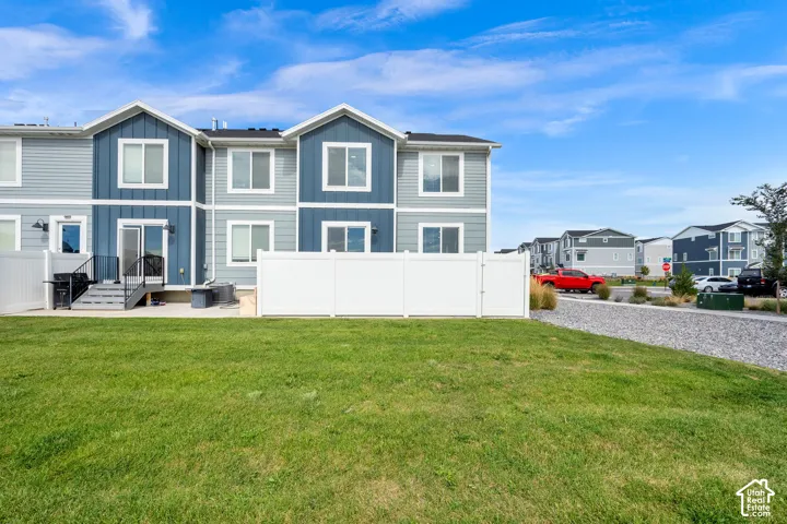 Rear exterior featuring a patio with steps, sliding glass door access, white privacy fencing, and an expansive grassy area