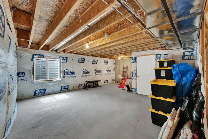 Unfinished basement featuring exposed wood joists, concrete flooring, a white window, and a white interior door