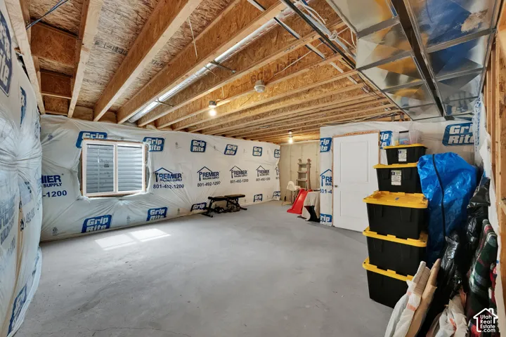 Unfinished basement featuring exposed wood joists, concrete flooring, a white window, and a white interior door
