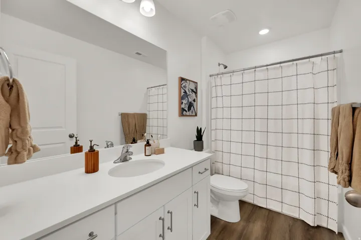 Bathroom featuring a single vanity with an undermount sink, a white countertop, coordinating white cabinetry with silver-tone hardware, and wood-finish flooring