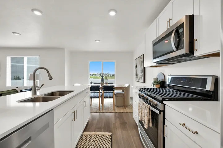 Kitchen featuring white cabinetry, stainless steel appliances, a double basin sink, light-toned countertops, and wood-finish flooring