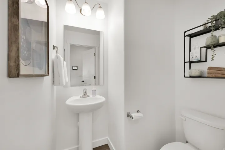 Pedestal sink, wall-mounted mirror, overhead vanity lighting, and a wall-mounted shelving unit