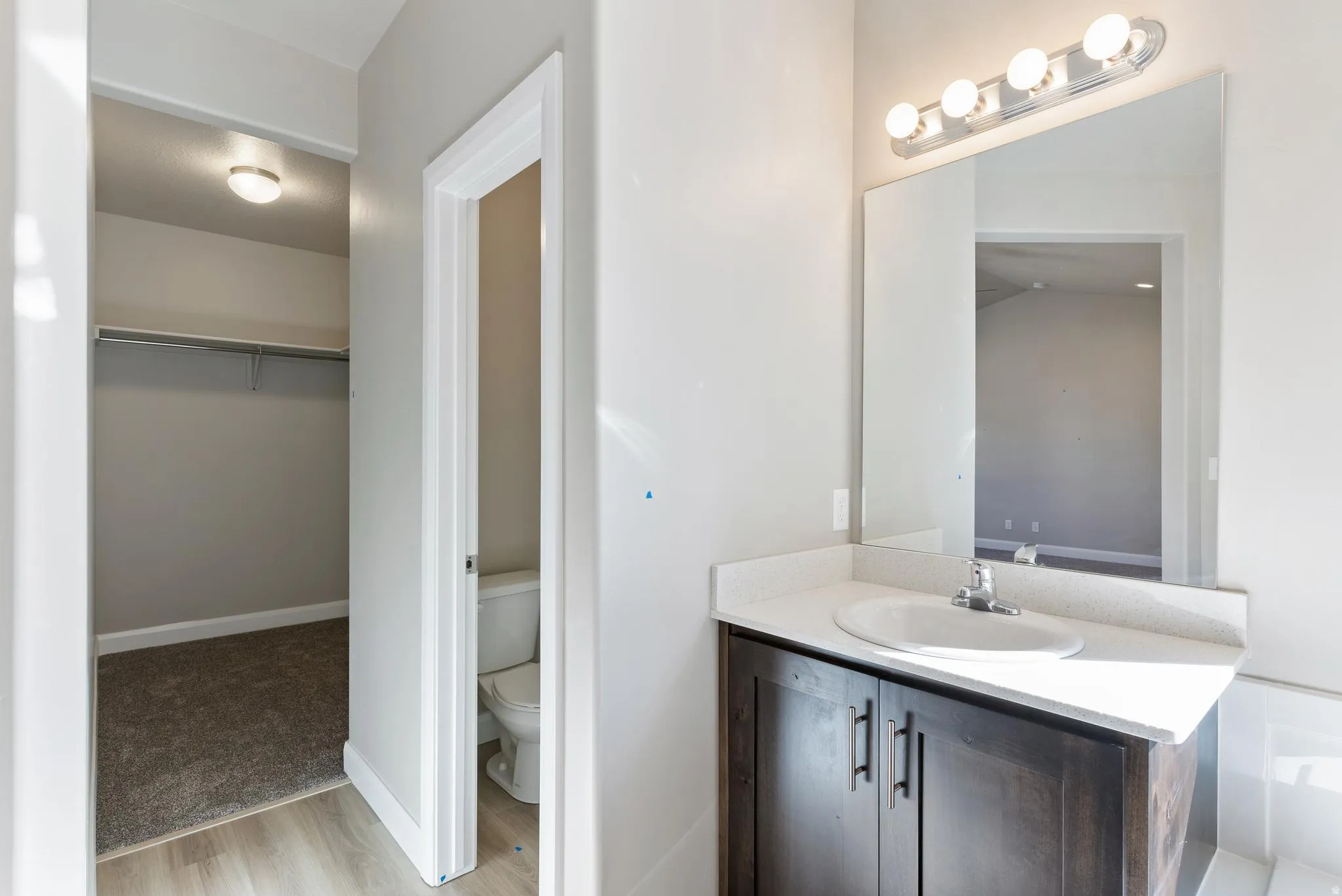 Dark wood-finish vanity with an integrated sink, light-toned countertop, and a large mirror with overhead lighting