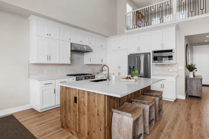 Kitchen featuring white cabinetry, wood-finish flooring, stainless steel appliances, a center island with a light-colored countertop, and a lofted space above