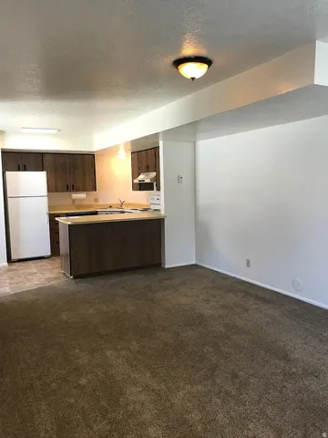 Open-concept living space featuring wood-finish cabinetry, light-toned countertops, a built-in microwave, and a white refrigerator
