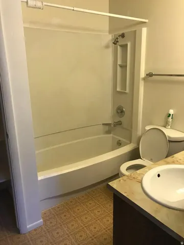 Built-in bathtub with integrated shower, vanity with an integrated sink, and patterned flooring