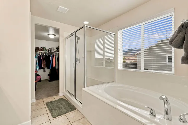 Tiled flooring, built-in soaking tub, glass-enclosed shower, window with blinds, recessed lighting