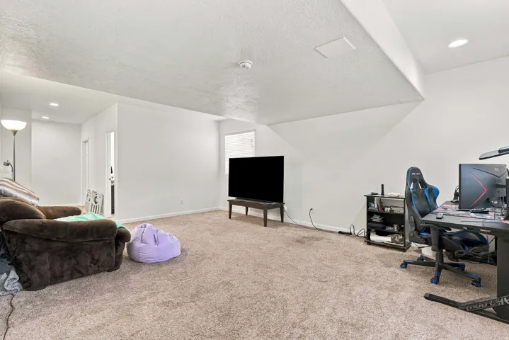 Spacious room featuring sloped ceilings, recessed lighting, and soft carpet flooring