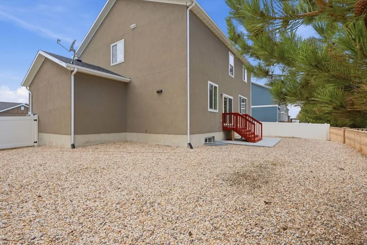 Stucco exterior with white trim, red exterior stairs, a concrete patio, and a gravel yard