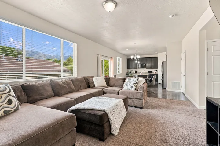 Spacious living area featuring carpet flooring, large windows with horizontal blinds, and a built-in ceiling light fixture