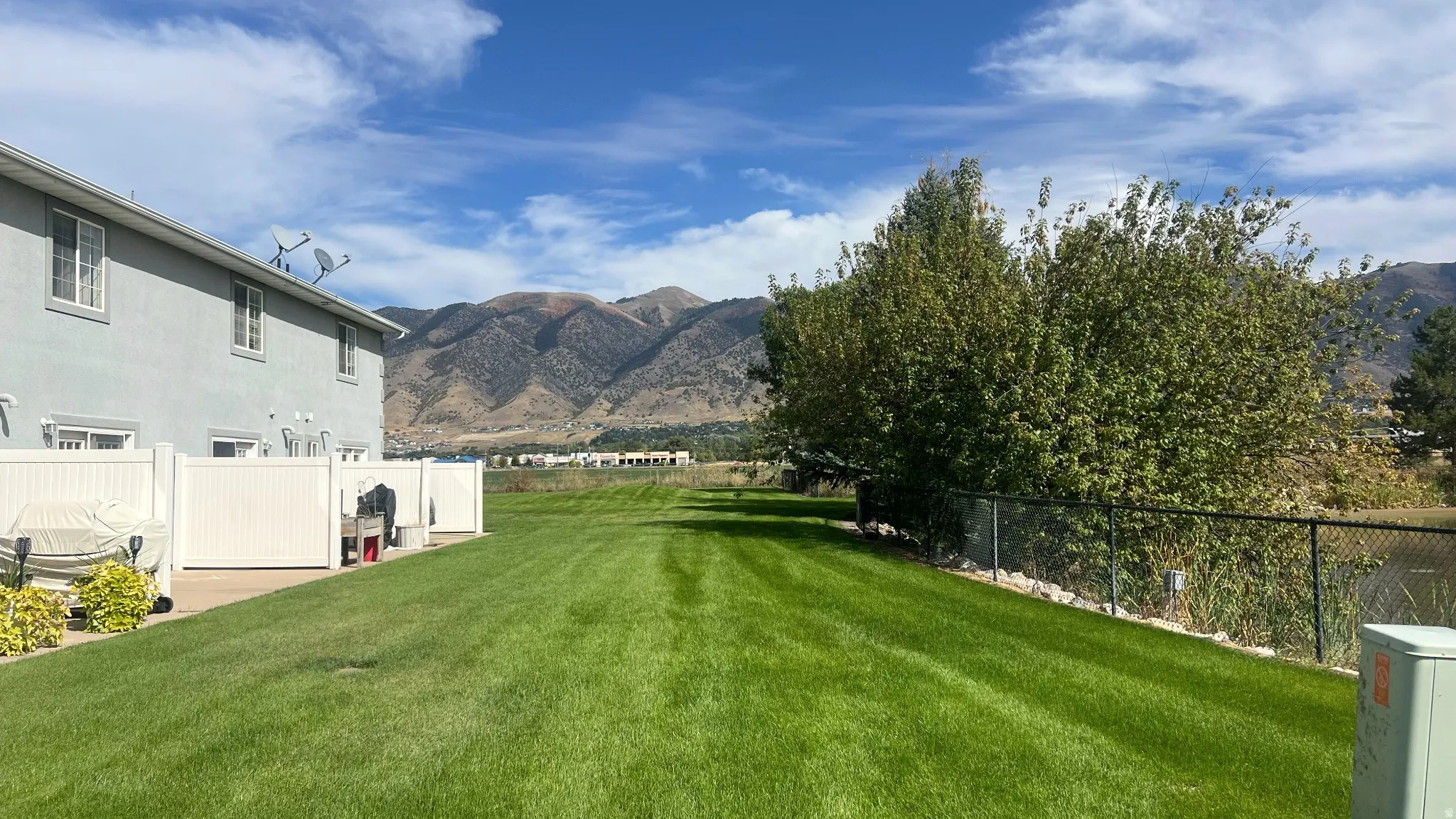Expansive green space with mountain backdrop, bordered by mature trees and a body of water