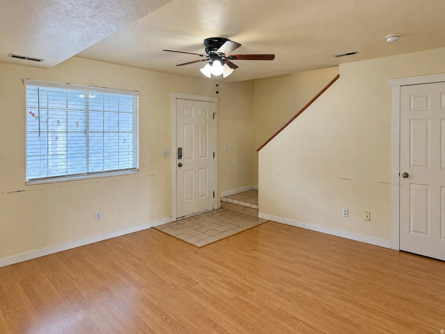Wood-finish flooring, ceiling fan with light fixture, window with blinds, and white paneled interior doors