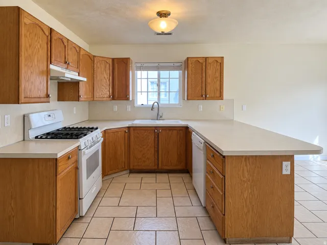 U-shaped kitchen featuring wood cabinetry, light-toned countertops, tile flooring, a gas range, and a window above the sink