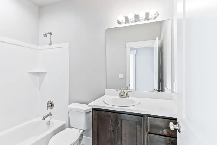 White bathtub with shower, toilet, and a vanity featuring a white countertop and dark wood-finish cabinetry