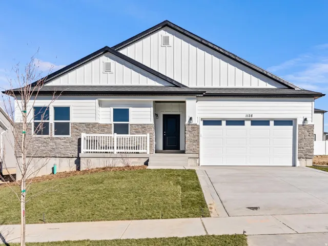 Contemporary home exterior with white siding, stone veneer accents, an attached two-car garage, covered porch with white railing, and a concrete driveway