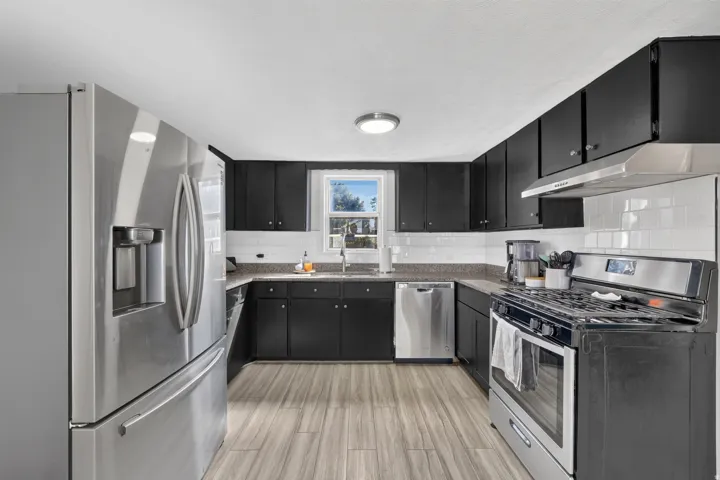 Kitchen featuring dark cabinetry, light-toned wood-finish flooring, stainless steel appliances, and a subway tile backsplash