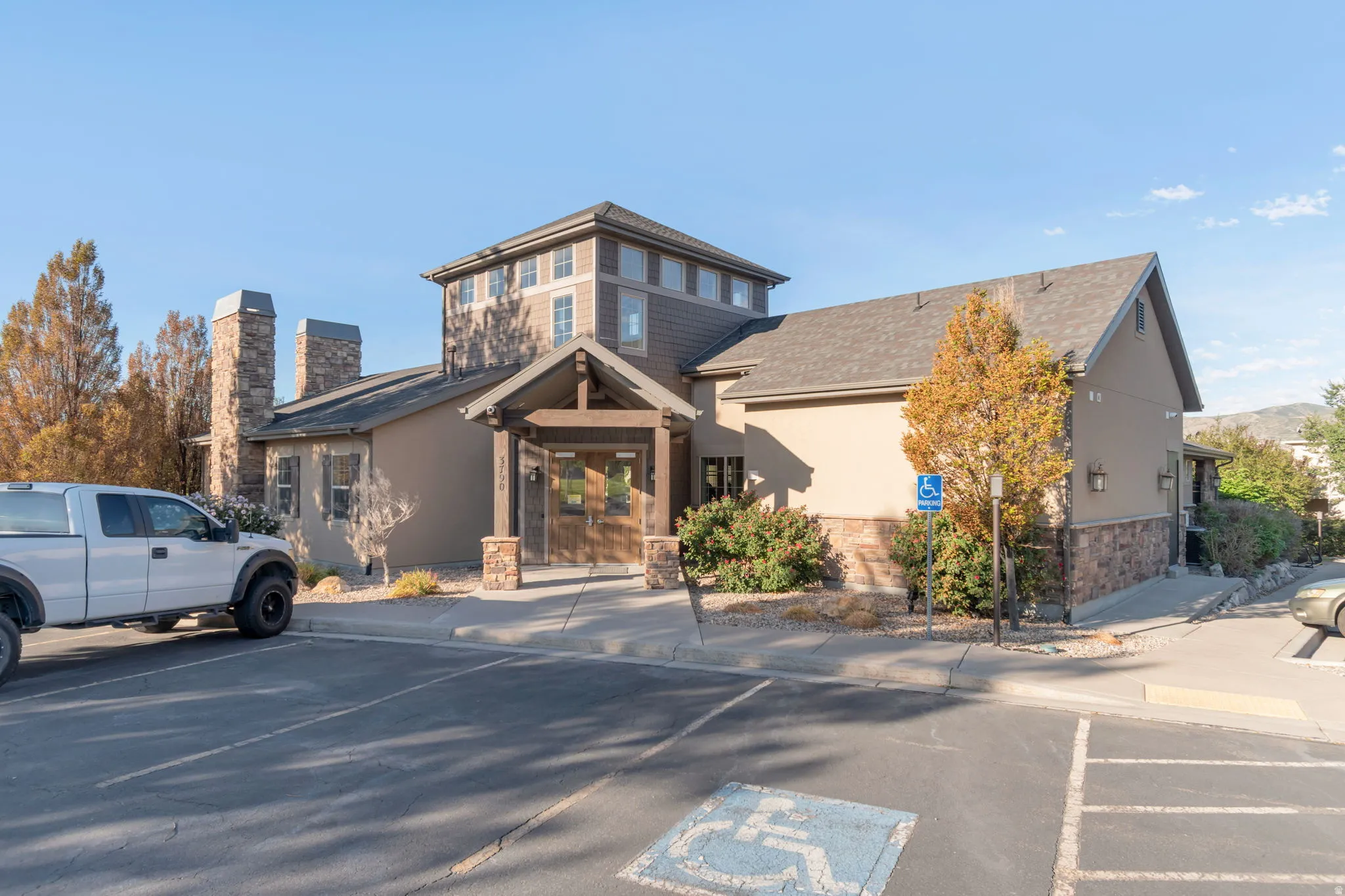 Club House nearby. Multi-level building with a stone-clad entry, wood detailing, prominent stone chimneys, and a paved parking area