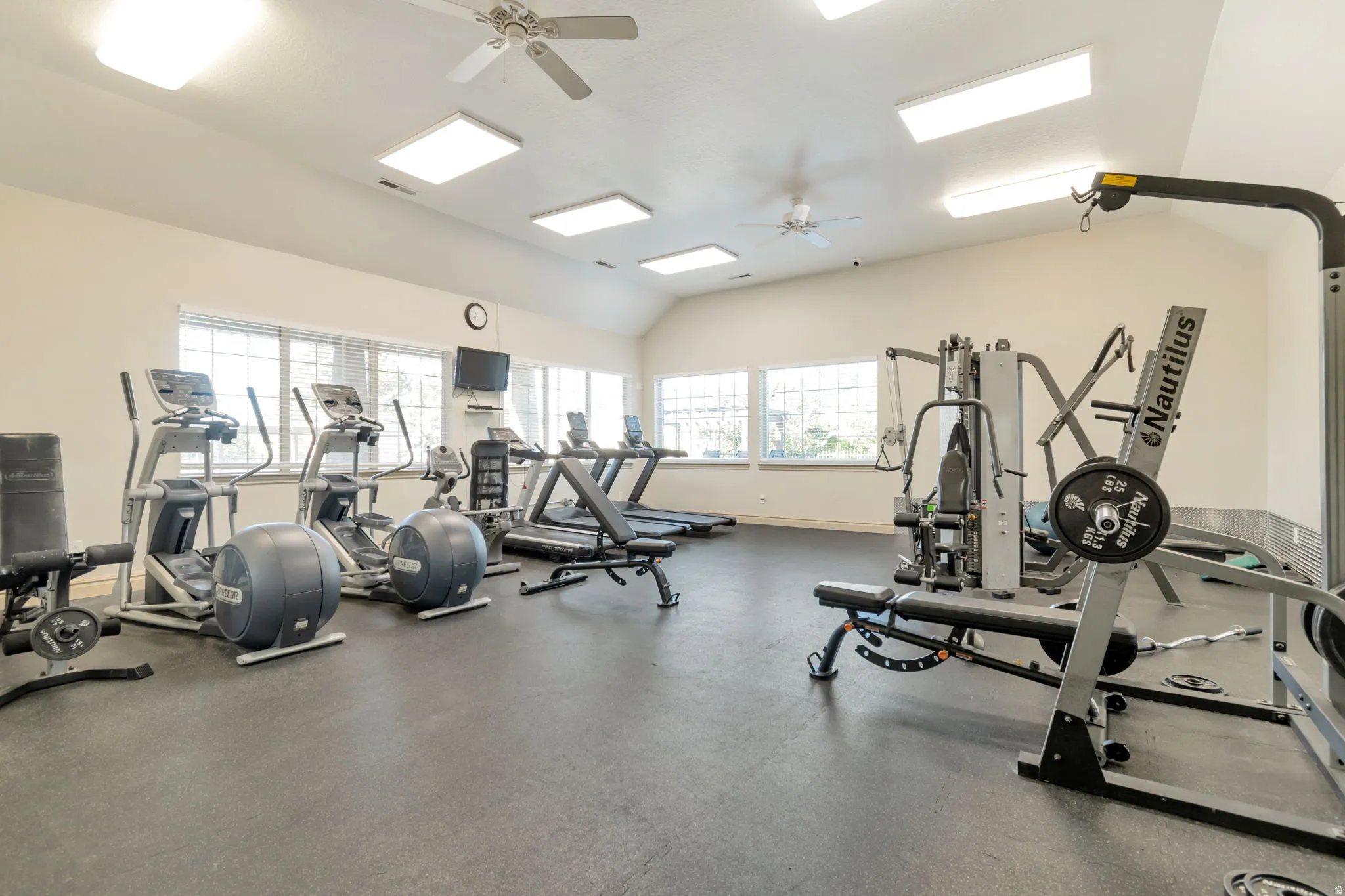 Fitness center featuring vaulted ceilings, ceiling fans, multiple windows, recessed lighting, and rubberized flooring