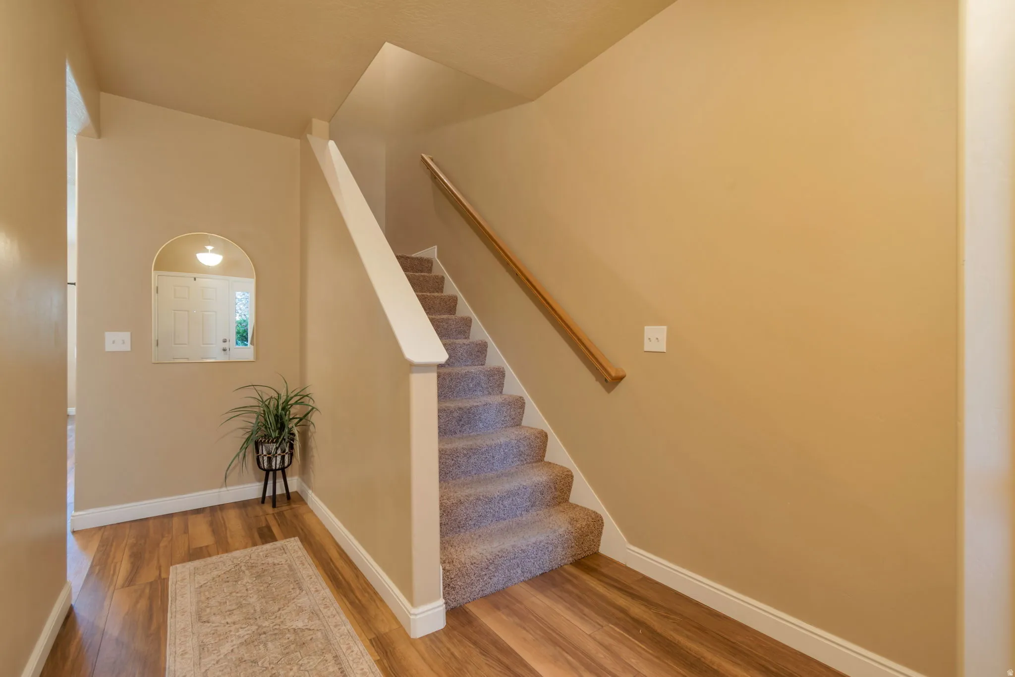 Wood-finish flooring with a carpeted staircase featuring a wood handrail