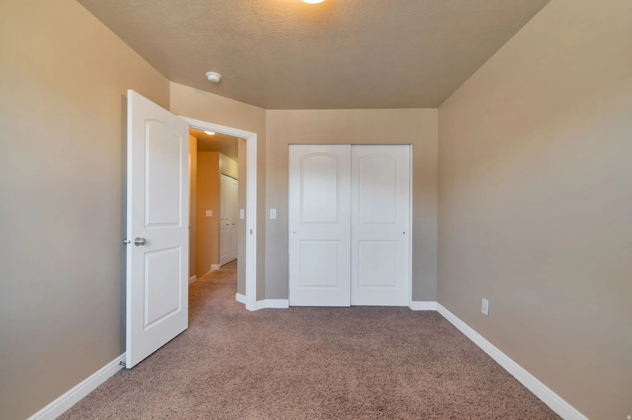 Neutral-toned walls, carpeted flooring, white trim, and a white bi-fold closet