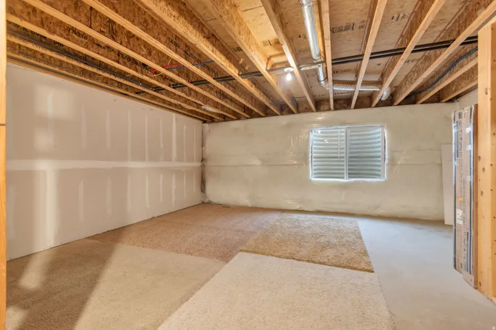 Future Family Room in Basement. Exposed ceiling joists with visible ductwork and wiring, partial drywall installation, insulated wall with a window well, and partial carpeting over a concrete floor